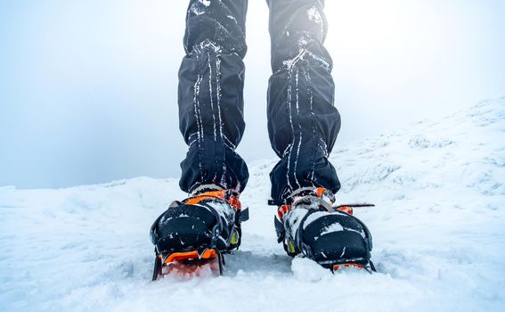 Man wearing crampons on trekking boots standing on snow