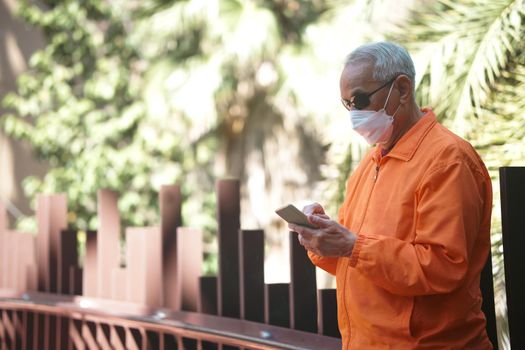 asian old elder senior man elderly wearing mask using mobile smart phone cellphone outdoor. mature retirement lifestyle