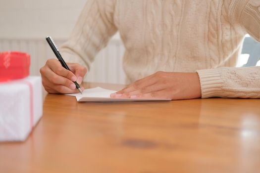 man wearing cream sweater writing christmas letter greeting card holiday wishes. xmas celebration.