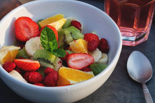 Fruit salad in a white bowl on a tray with a drink and a spoon.