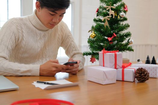 man wearing cream sweater using mobile smart phone with christmas decoration. xmas new year holiday celebration.