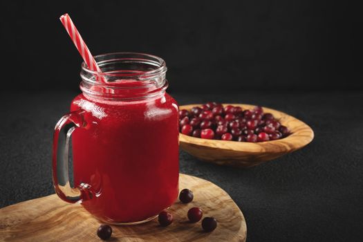 Healing cranberry juice in a glass jar-mug with a straw on black table. Healthy eating concept.