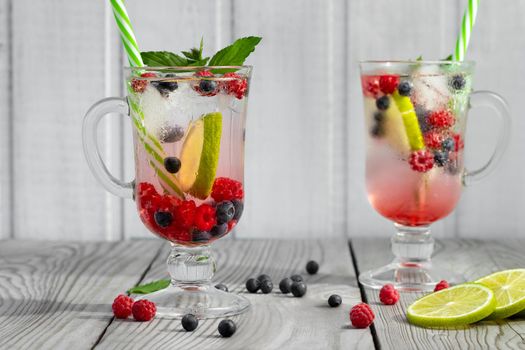 Fresh homemade summer cocktails with ice, lime and berries in glasses with a straw.