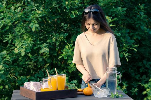 Girl cooking summer orange cocktail with mint and ice cubes outdoors, selective focus.