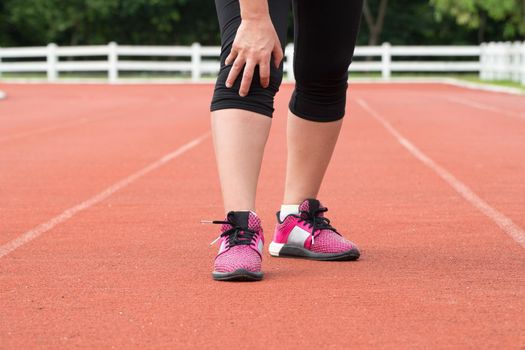 Middle aged woman runner knee pain during training outdoors.