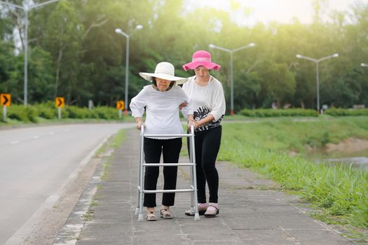 Daughter take care elderly woman walking on street in strong sunlight.