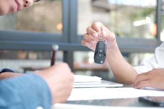 dealer salesman giving car key to new owner. client signing insurance document or rental car lease form