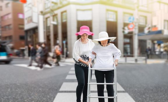 Daughter take care elderly woman walking across the street in downtown