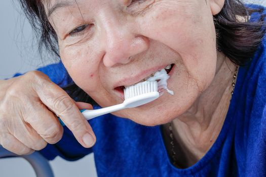 Asian elderly woman trying use toothbrush ,hand tremor . Dental health