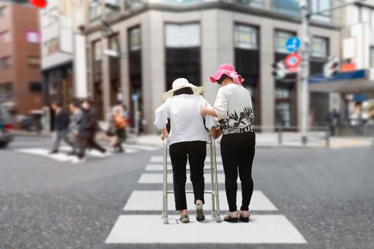 Daughter take care elderly woman walking on street in strong sunlight.