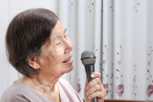 Elderly woman sing a song on microphone at home.