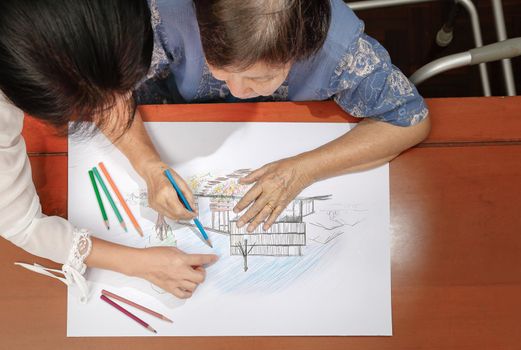 Elderly woman painting color on her drawing with daughter , hobby at home