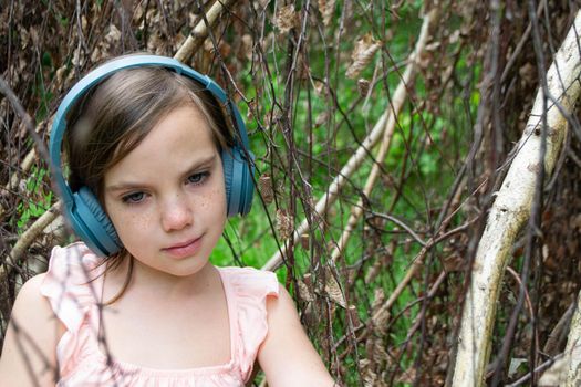 Young beautiful girl fooling around with a branch and wearing headphones on them to listen to music or block out sound due to auditory sensitivity. High quality photo