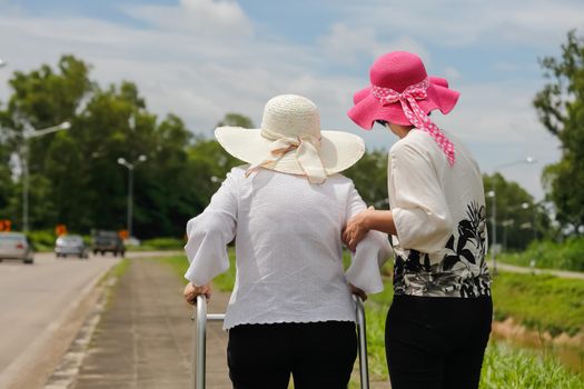 Daughter take care elderly woman walking on street in strong sunlight.