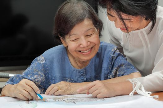 Elderly woman painting color on her drawing with daughter , hobby at home