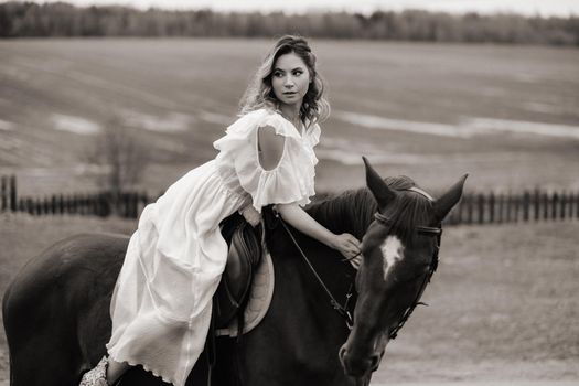 A woman in a white sundress riding a horse in a field. black and white photo.