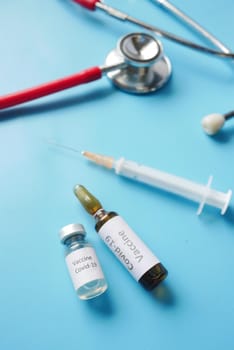 Close up of coronavirus vaccine , stethoscope and syringe on blue ,