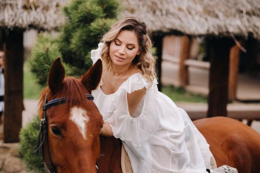 A woman in a white sundress riding a horse near a farm.