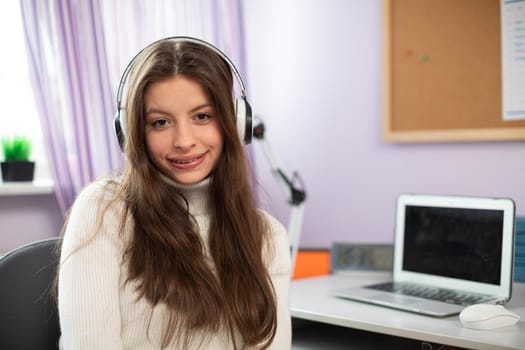 Teenage girl laughs into camera while listening to music on wireless headphones. Attractive girl with long hair.