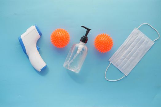 Surgical masks, thermometer and hand sanitizer on blue background .