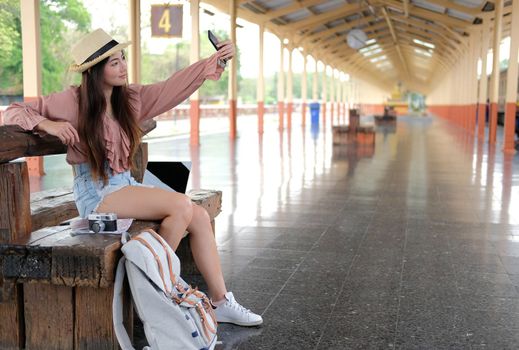 asian woman use smart phone to take selfie photo at train station. traveler travel on holiday