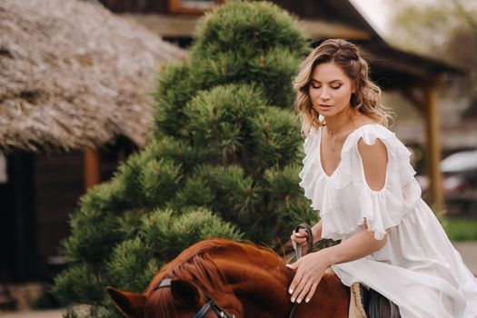 A woman in a white sundress riding a horse near a farm.