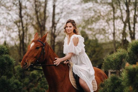 A woman in a white sundress riding a horse near a farm.