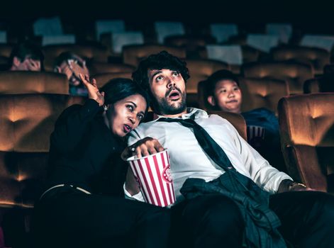 Audience sitting in a cinema and watching terrible horror. Afraid woman sitting near a man is shock and scare