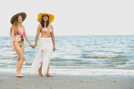 Happy women in bikinis go sunbathing together on tropical sand beach in summer vacation. Travel lifestyle.