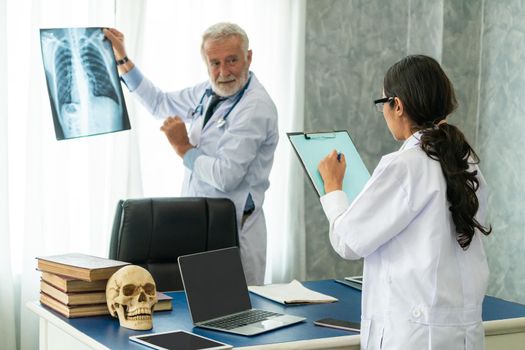 Senior male doctor looking at x ray film of patient chest injury while working with another doctor at the hospital. Medical healthcare staff and doctor service.