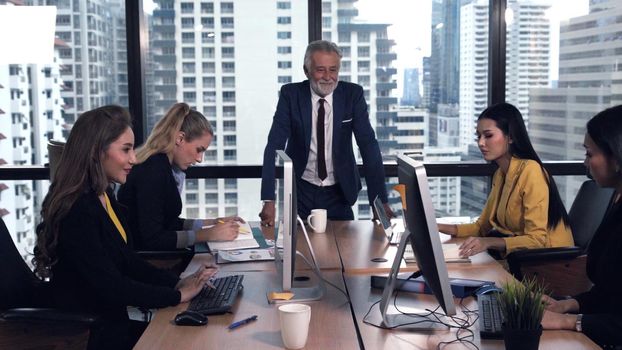 Senior leader giving advice speech to team members. Creative business people meeting at table in modern office. Multicultural business team.