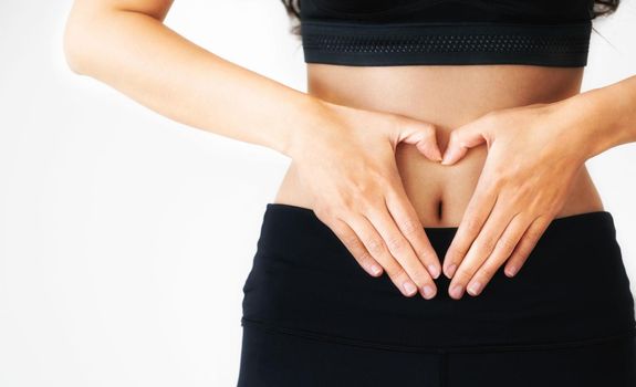 Close up shot of young woman in sportswear making heart shape gesture at her abdomen. Dieting weight loss and healthy nutrition concept.