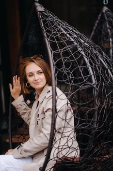 A happy stylish girl In a gray coat is sitting outside in an armchair.