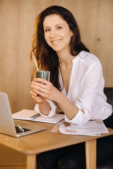 A young freelance woman with a cocktail in her hands at her workplace at work.