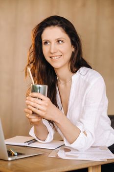 A young freelance woman with a cocktail in her hands at her workplace at work.