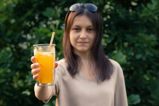 Beautiful girl holds out a glass with a fresh orange summer cocktail, selective focus.