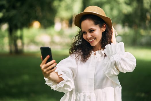 Young beautiful girl in a hat makes a selfie on her phone in the park. High quality photo