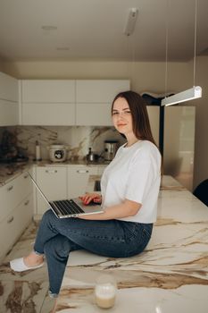 Young woman working from home office. Freelancer using laptop and the Internet for shopping online. Happy girl smiling. Workplace in cozy kitchen. Successful female business. Lifestyle moment