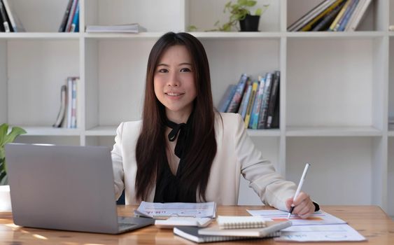 Charming Asian woman working at the office using a laptop Looking at the camera..