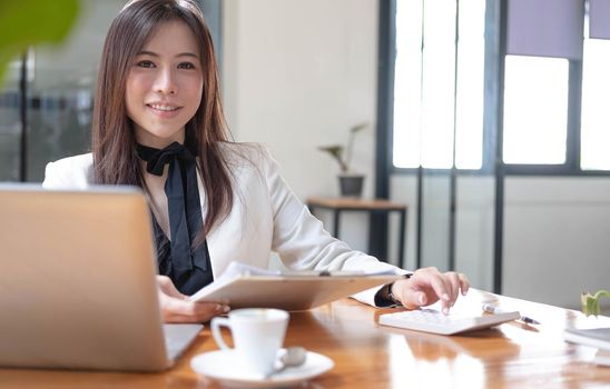 Beautiful smiling Asian businesswoman hand holding pen working using tablet at office. Looking at camera..