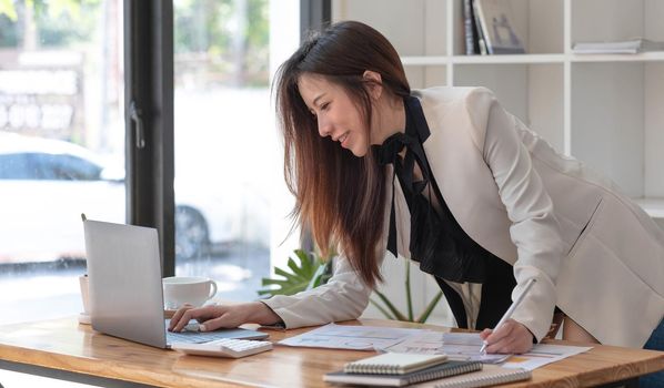 Happy young Asian businesswoman standing using laptop computer at office..