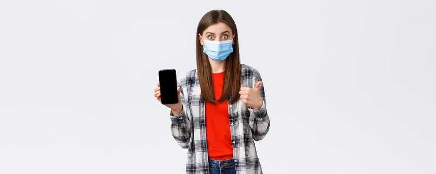 Different emotions, covid-19, social distancing and technology concept. Excited young happy woman recommend good app, show mobile phone screen and thumb-up, wear medical mask.