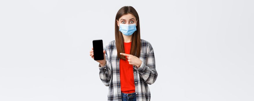 Different emotions, covid-19, social distancing and technology concept. Interested and excited woman in medical mask pointing finger mobile phone screen, promote app or order on shopping site.