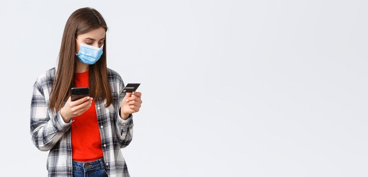 Coronavirus outbreak, working from home, online shopping and contactless payment concept. Girl in medical mask pay order groceries from grocery store to deliver, hold mobile phone and credit card.