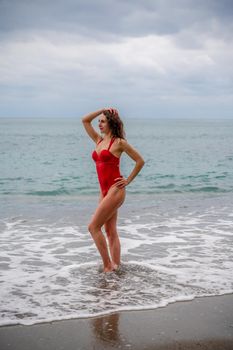 A beautiful and sexy brunette in a red swimsuit on a pebble beach, Running along the shore in the foam of the waves.