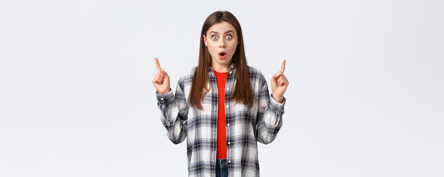 Lifestyle, different emotions, leisure activities concept. Astonished and speechless attractive girl in checked shirt pointing fingers up to tell news, drop jaw staring, make wow expression.