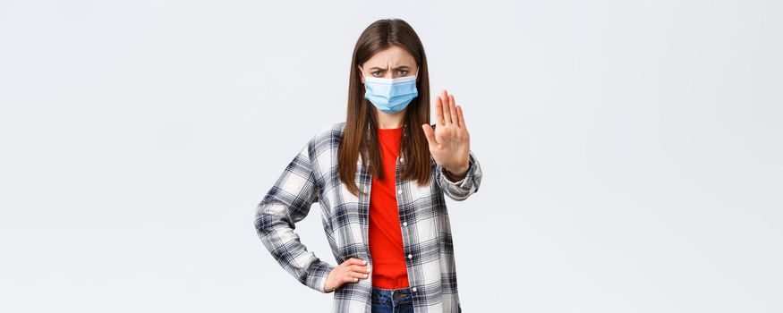 Coronavirus outbreak, leisure on quarantine, social distancing and emotions concept. Young woman in medical mask look disappointed, disapprove smth, show stop or prohibition gesture.
