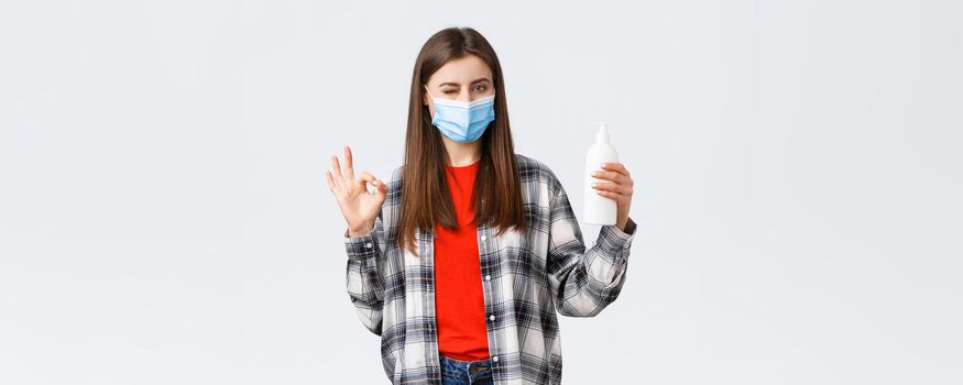 Coronavirus outbreak, leisure on quarantine, social distancing and emotions concept. Cute caucasian woman in medical mask assure this soap is good for preventing virus, show oka sign.