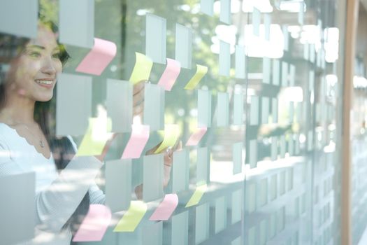 businesswoman woman thinking planning with adhesive notes on glass wall at workplace. Sticky note paper reminder schedule for creative idea & business brainstorming