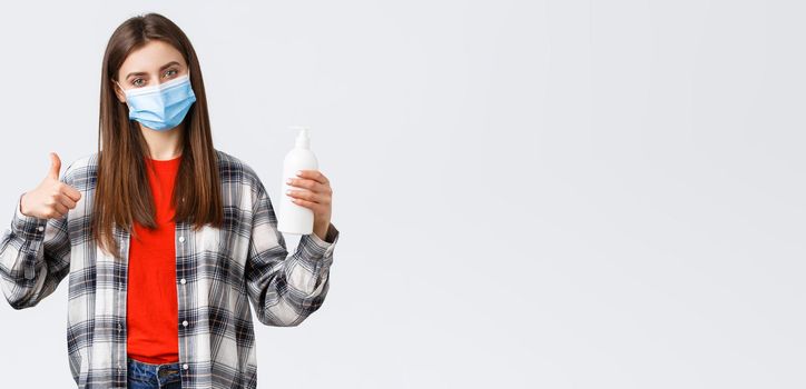 Coronavirus outbreak, leisure on quarantine, social distancing and emotions concept. Satisfied female customer, shop client in medical mask advice this hand soap or hand sanitizer, thumb-up.